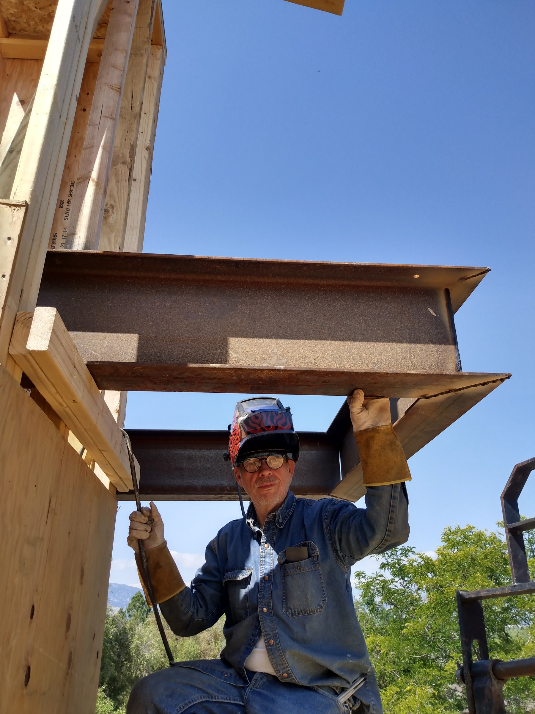Jose Trevino in welding gear steadying a steel I-beam overhead on a build site
